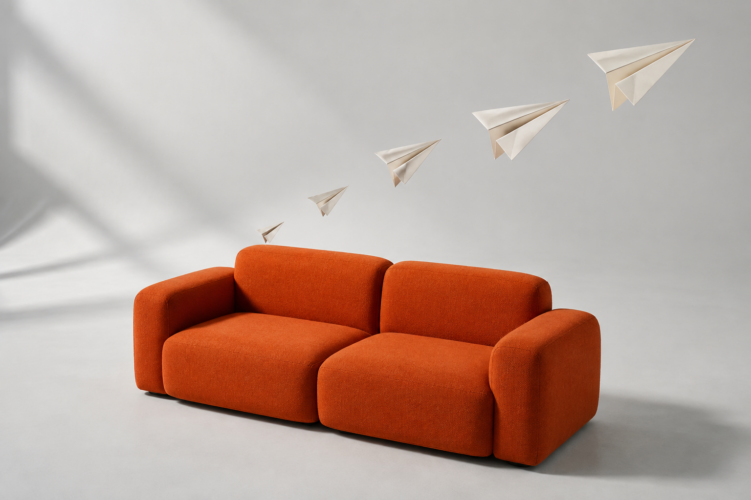 Paper airplanes taking flight above a sculptural orange couch.